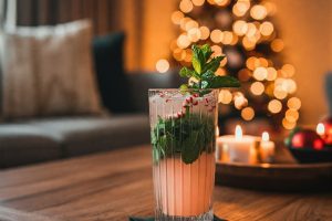 Holiday mocktail in a coupe glass with a candy cane garnish, held in a cozy gathering.